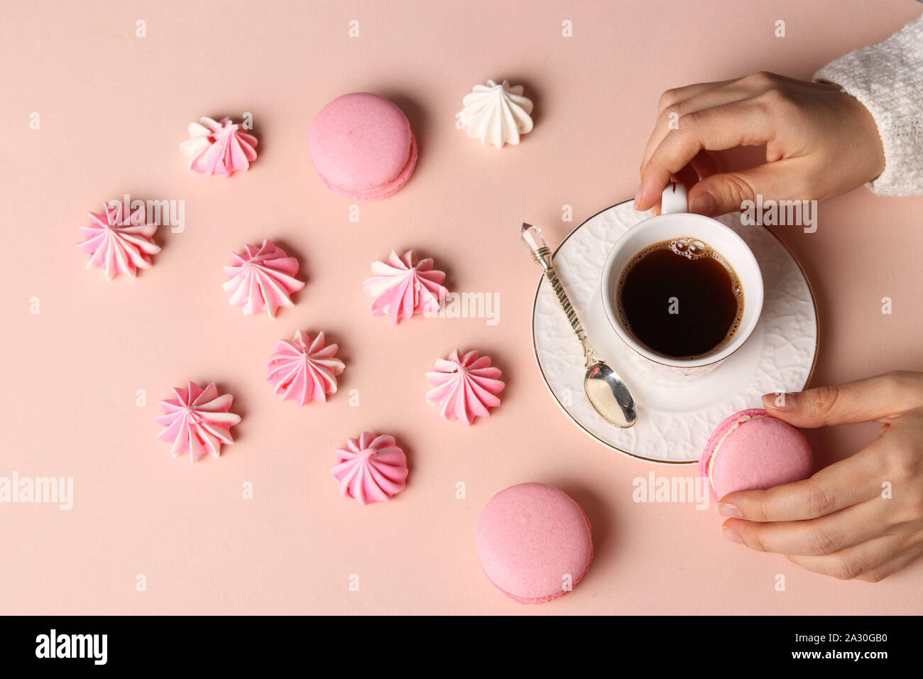 Baiser Plätzchen und Makronen auf einem rosa Hintergrund, Tasse Kaffee und Frauen Hände Stockfoto