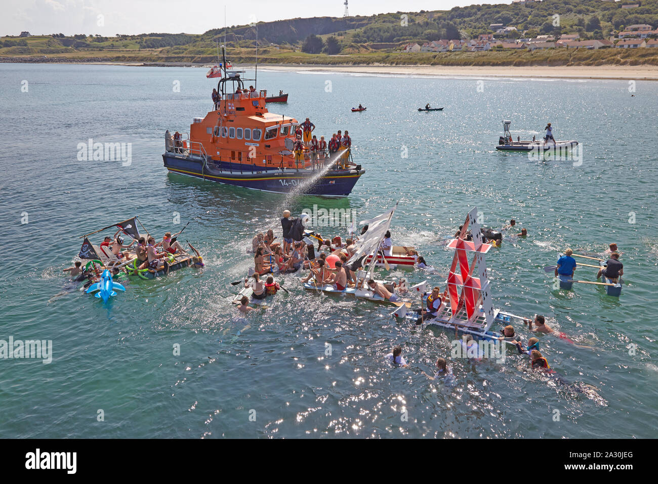 Lifeboatman abspritzen Wasser bei Daft floss Rennen Teilnehmer während des jährlichen Festivals namens Alderney Woche in Alderney auf den Kanalinseln, GB Stockfoto