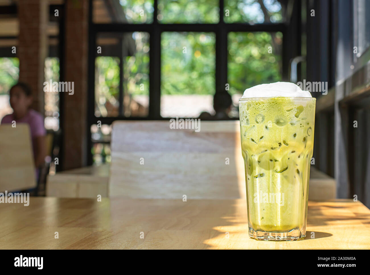 Eistee grüner Tee im Glas auf dem hölzernen Tisch Hintergrund Glasfenster und Baum. Stockfoto