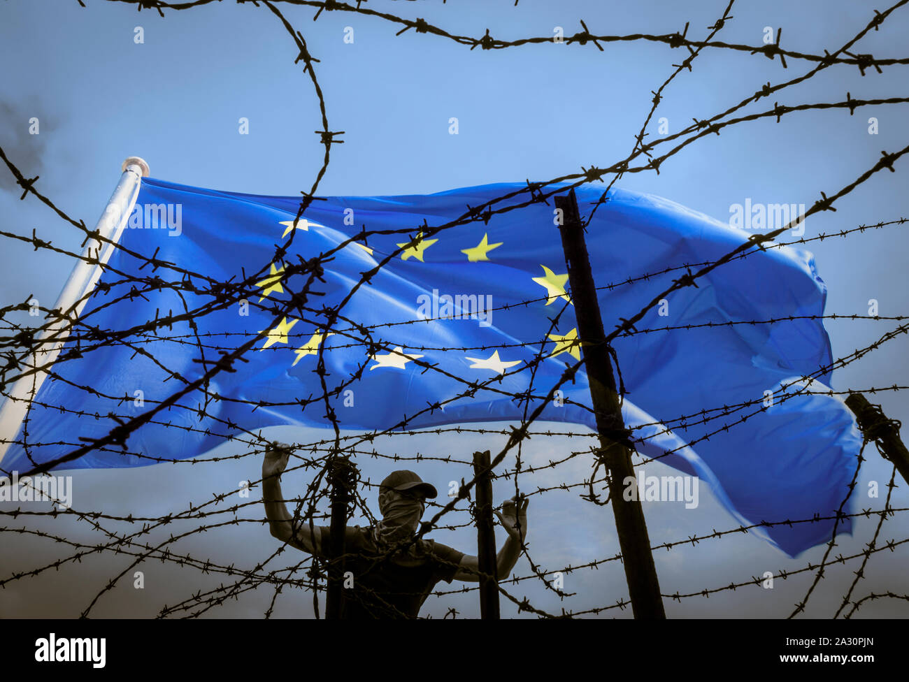 Brexit, Immigration, Asylbewerber... Konzeptbild. Mann, der unter EU-Flagge durch Stacheldrahtzaun blickt. Stockfoto