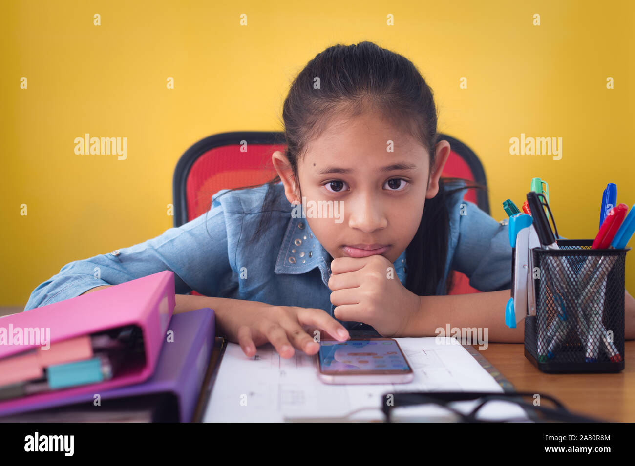 Nettes Mädchen mit Handy auf dem Schreibtisch isoliert gelben Hintergrund. Konzept der Leistung. Stockfoto