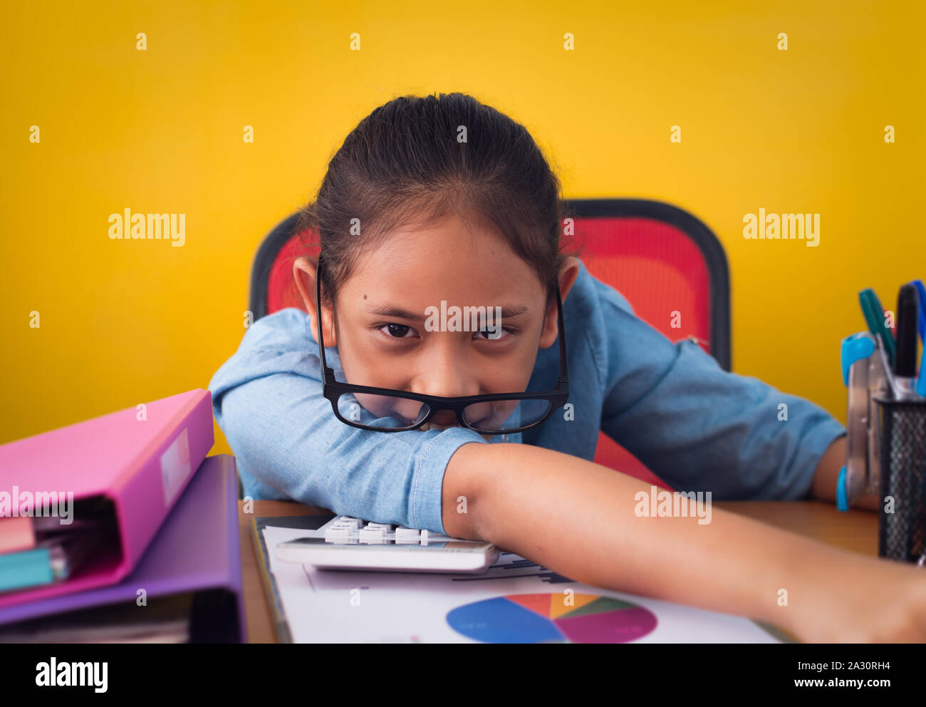 Lustige süße Mädchen Arbeiten am Schreibtisch mit Dokument isoliert gelben Hintergrund. Konzept der Leistung. Stockfoto