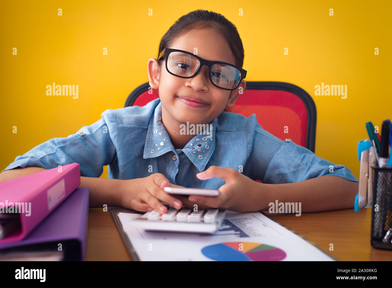 Süße Mädchen lächelnd und mit Handy am Schreibtisch isoliert gelben Hintergrund, Bildung Konzept. Stockfoto