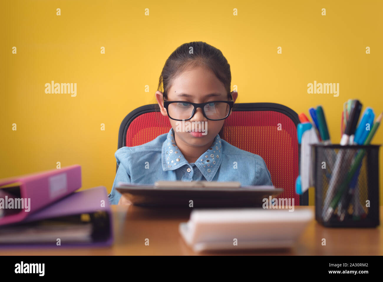 Süße Mädchen Brille arbeiten mit Dokument auf dem Schreibtisch auf gelbem Hintergrund, Bildung Konzept. Stockfoto