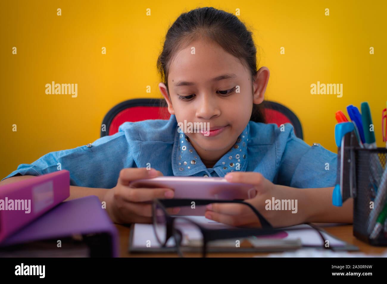 Süße Mädchen lächelnd und mit einem Handy am Schreibtisch isoliert gelben Hintergrund, Bildung Konzept. Stockfoto