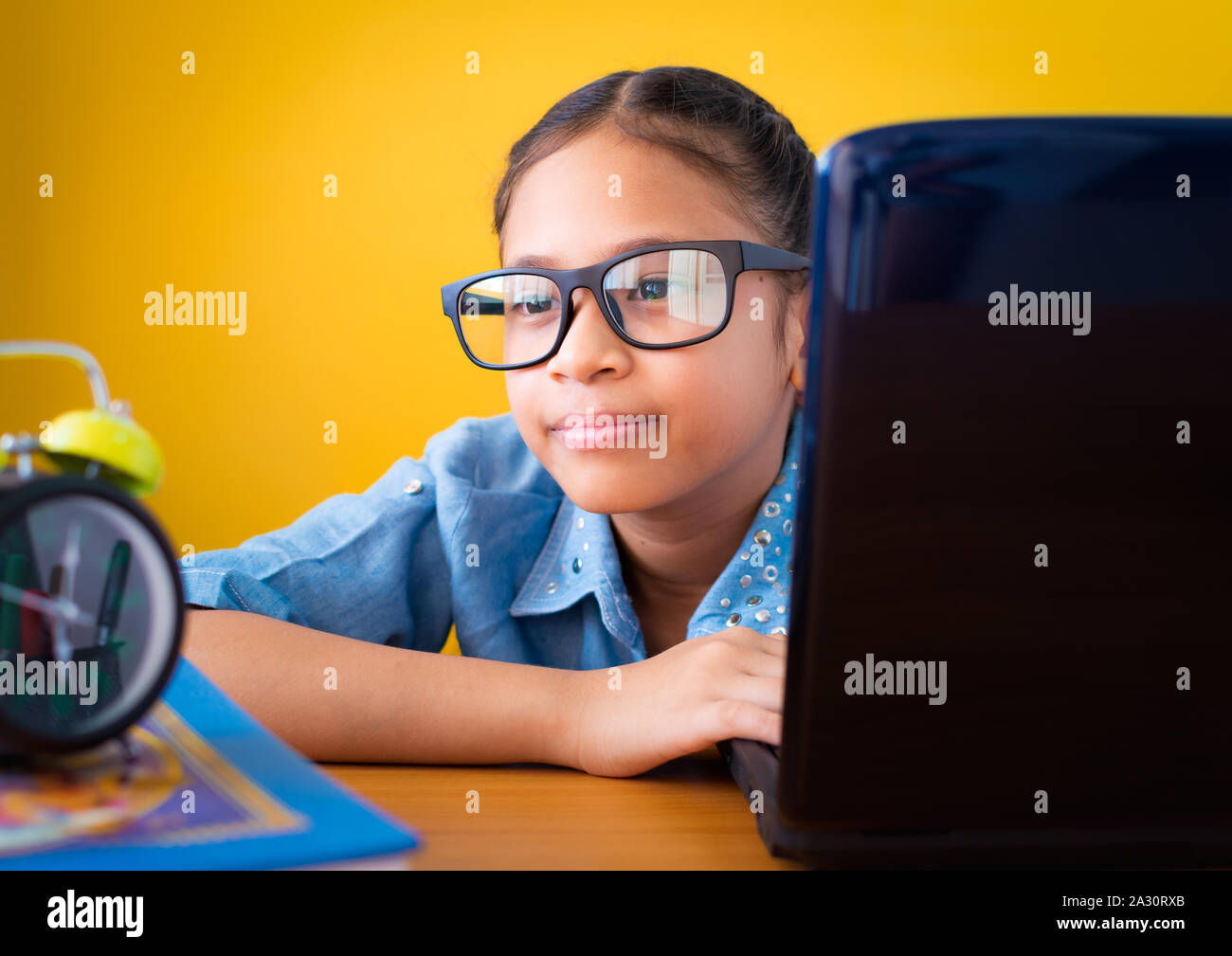 Süße Mädchen Tragen einer Brille mit Laptop auf dem Schreibtisch isoliert gelben Hintergrund, Bildung Konzept. Stockfoto