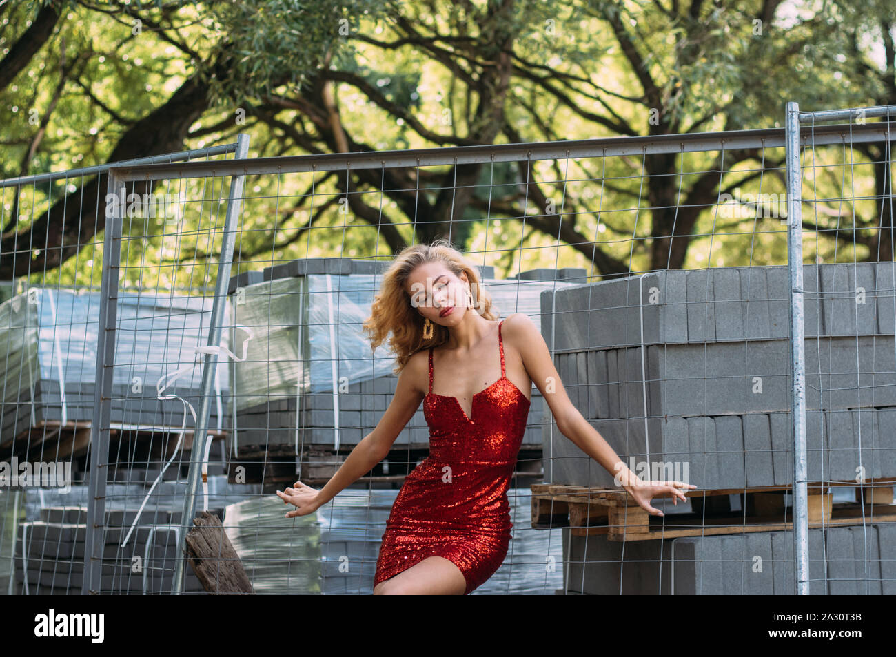 Schöne blonde Mädchen mit geschlossenen Augen in rot kurzes Kleid mit Pailletten im Park in der Nähe der Baustelle Stockfoto