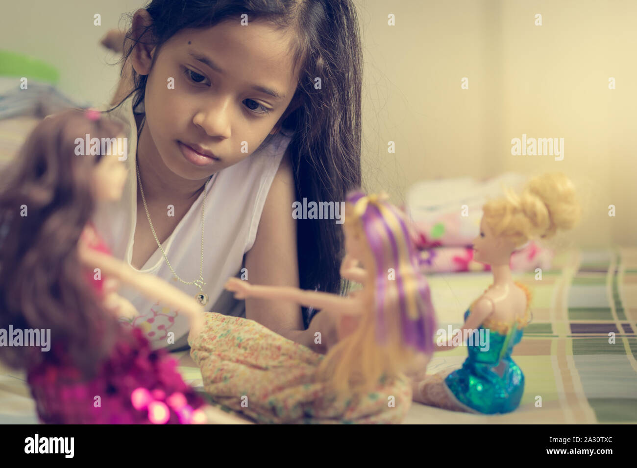 Kleine Mädchen spielen Puppen auf Bett im Urlaub. Stockfoto