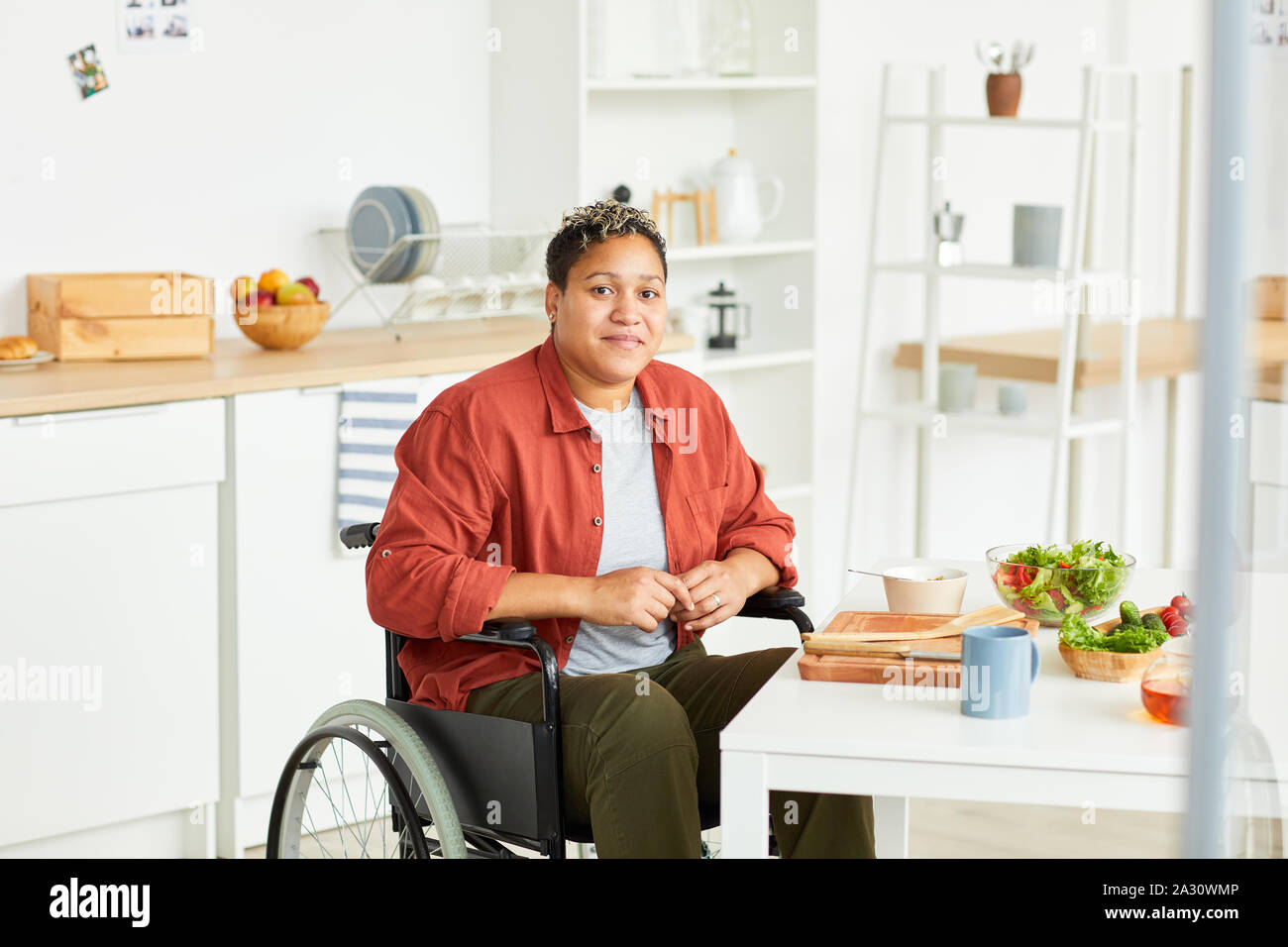 Portrait der Afrikanischen jungen behinderten Frau sitzt im Rollstuhl und mit Blick auf die Kamera in der Küche zu Hause. Stockfoto