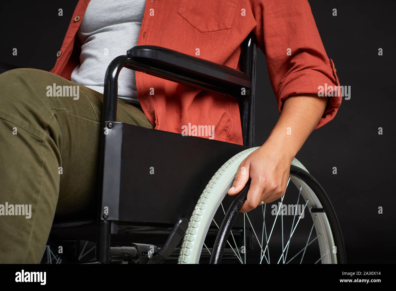 Nahaufnahme der jungen Frau in Freizeitkleidung Holding das Rad der Rollstuhl und Reiten auf ihm über schwarzen Hintergrund Stockfoto