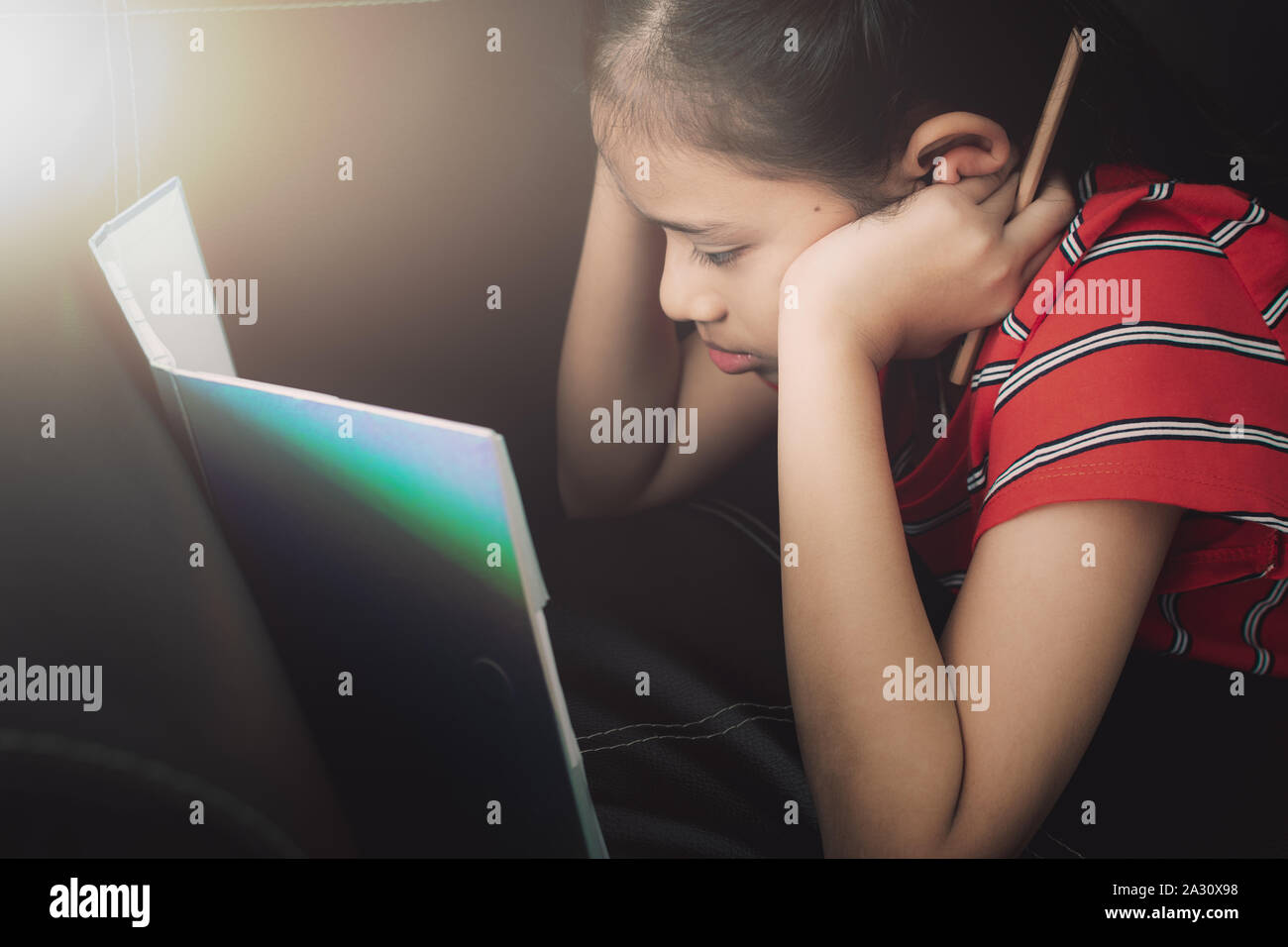 Kleines Mädchen mit Hausaufgaben auf dem Schlafsofa unter Licht zu Hause. Bildung Konzept. Stockfoto