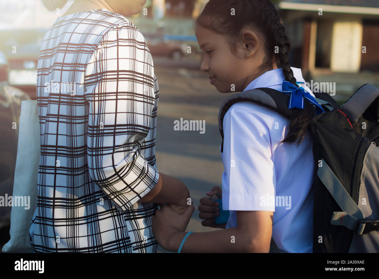 Mutter und Tochter gehen Hand in Hand unter Sonnenlicht in die Schule. Stockfoto