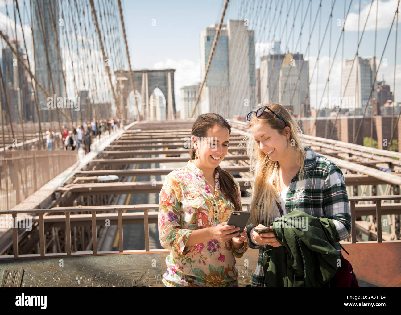 Zwei 20 Jahre alte weibliche Touristen vergleichen Handy Fotos auf der Brooklyn Bridge In New York City, USA. Stockfoto