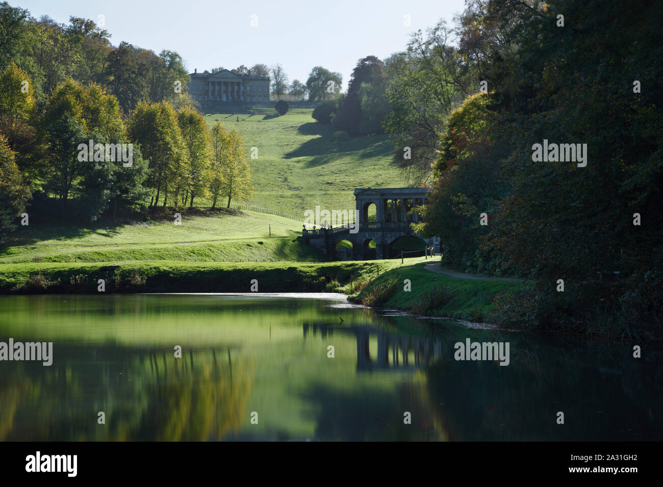 Vor Park Landschaft Garten. Blick auf die Palladianische Brücke und das Haus von den unteren See. Badewanne. UK. Stockfoto