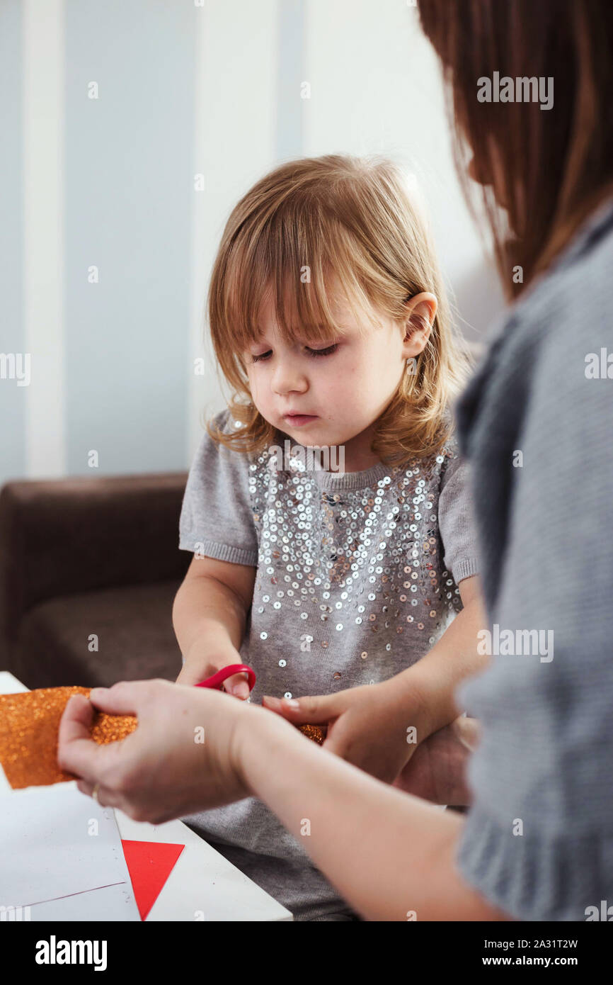 3-jähriges Mädchen und ihre Mutter eine Weihnachtsgirlande mit rotem glitter Papier. Lifestyle Bild, geringe Tiefenschärfe. Stockfoto