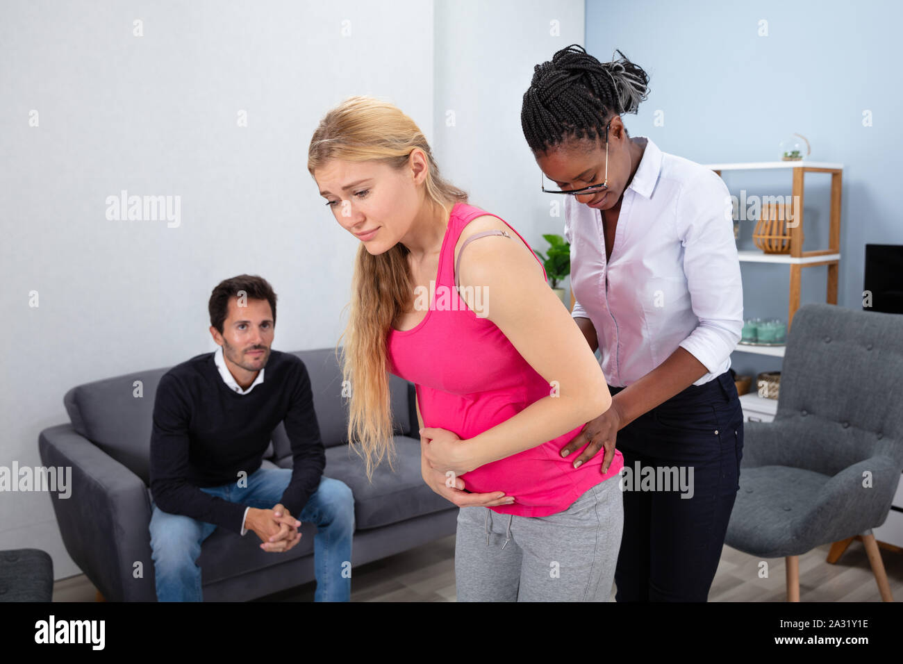 Mann sitzt auf einem Sofa an afrikanischen Frauen Massieren eine schwangere Frau leidet unter Schmerzen suchen Stockfoto