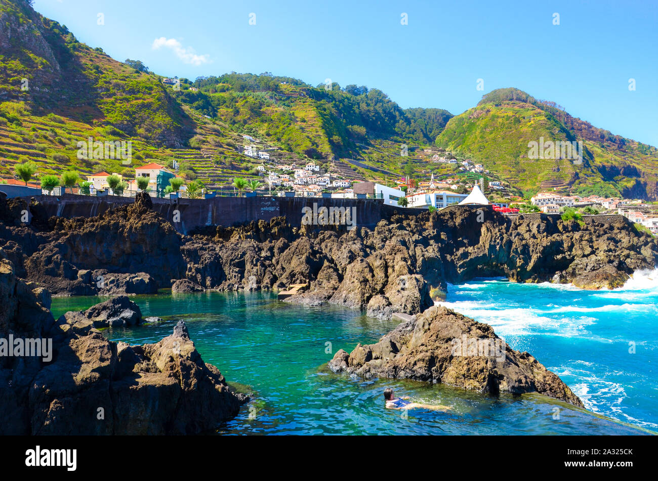 Frau Schwimmen in natürlichen Pools im Atlantischen Ozean, Insel Madeira, Portugal. Aus vulkanischem Gestein, in das Meer natürlich fließt. Dorf Porto Moniz an der felsigen Hügel im Hintergrund. Stockfoto