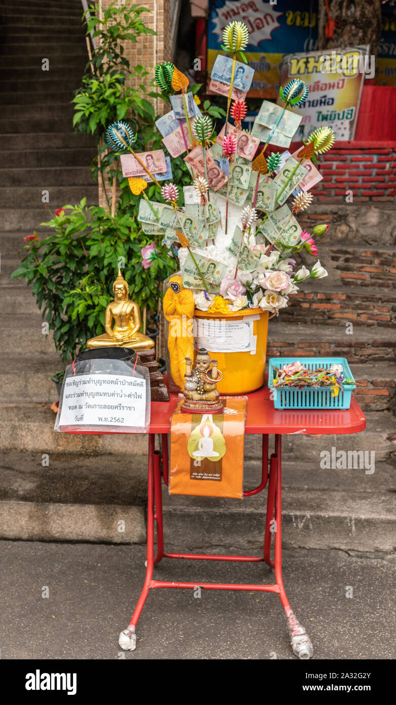 Si Racha, Thailand - 16. März 2019: Gelbe Spendenbox Vase mit kleinen Statuen auf dem roten Tisch Treppe gesetzt Wat Koh Loy buddhistischen Schreine in der h Stockfoto