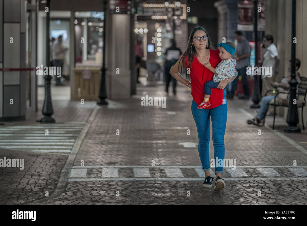 Eine einzelne Frau trägt ein rotes T-Shirt und Blue Jeans trägt, ihre Tochter beim Gehen auf eine saubere Straße. Stockfoto