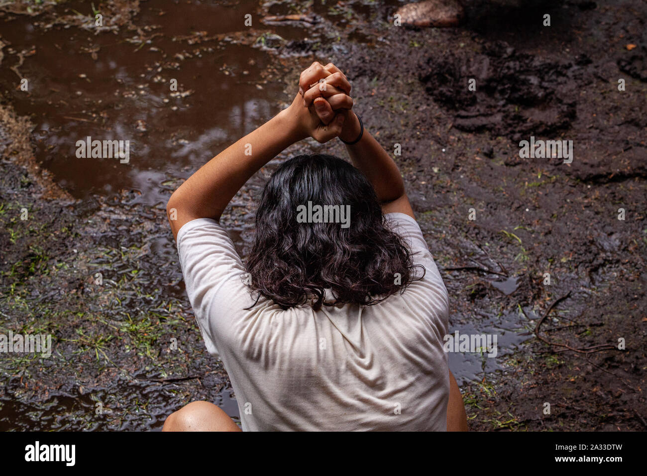 Eine junge weiße Frau gesehen wird, beten mit den Händen oben neigte ihren Kopf, als sie in einer schlammigen Pfütze hockt, die Betrachtung der Natur. Stockfoto Eine junge weiße Frau gesehen wird, beten mit den Händen oben neigte ihren Kopf, als sie in einer schlammigen Pfütze hockt, die Betrachtung der Natur. Stockfoto