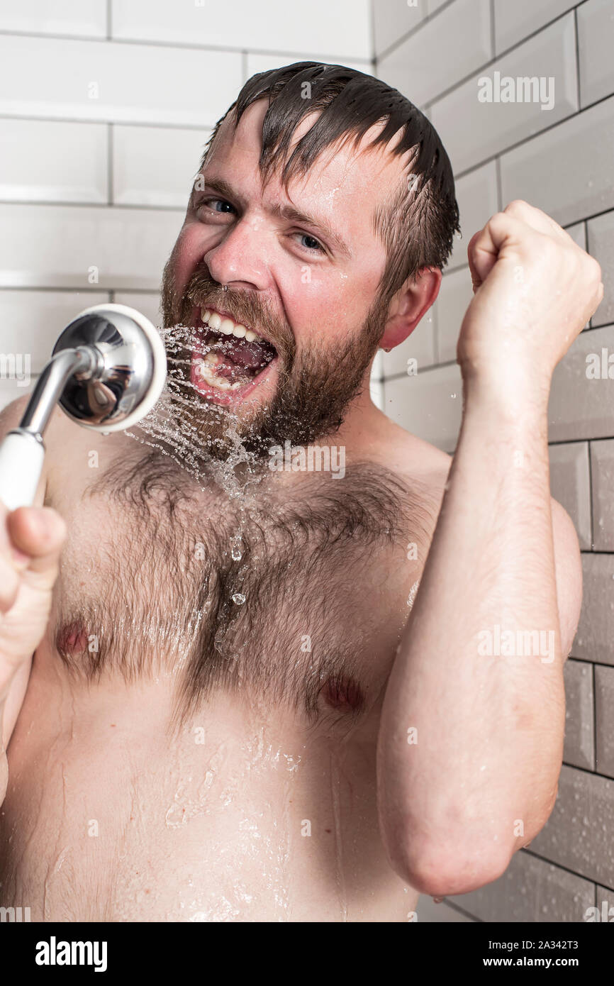 Cute bärtiger Mann singen im Badezimmer mit der Dusche mit fließendem Wasser anstelle von einem Mikrofon. Stockfoto