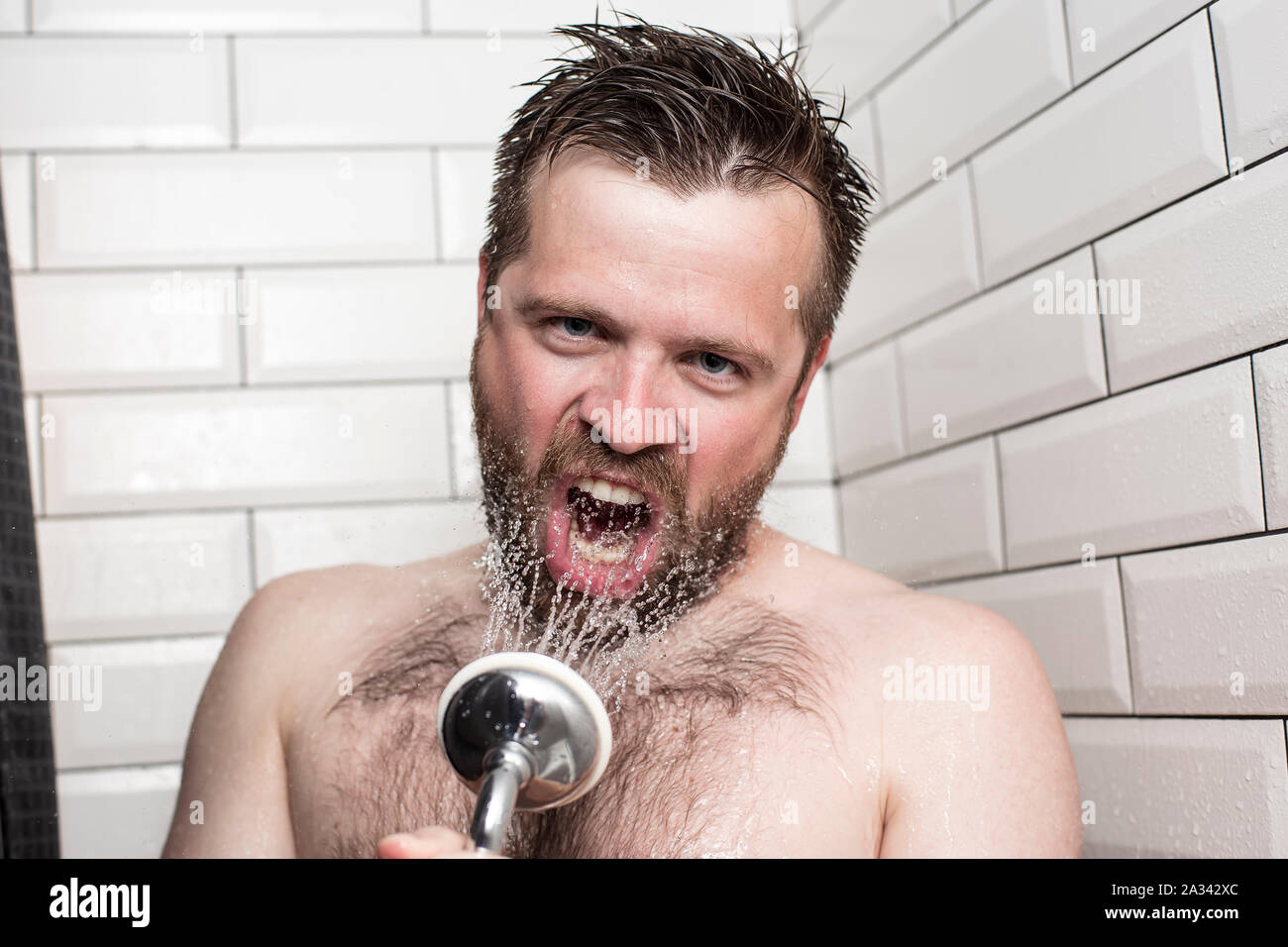 Cute bärtiger Mann singen im Badezimmer mit der Dusche mit fließendem Wasser anstelle von einem Mikrofon. Stockfoto