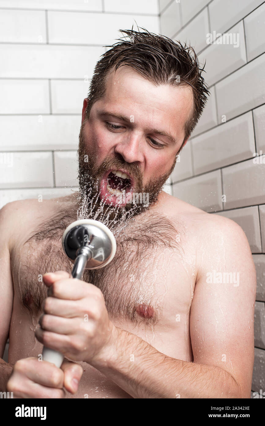 Cute bärtiger Mann singen im Badezimmer mit der Dusche mit fließendem Wasser anstelle von einem Mikrofon. Stockfoto