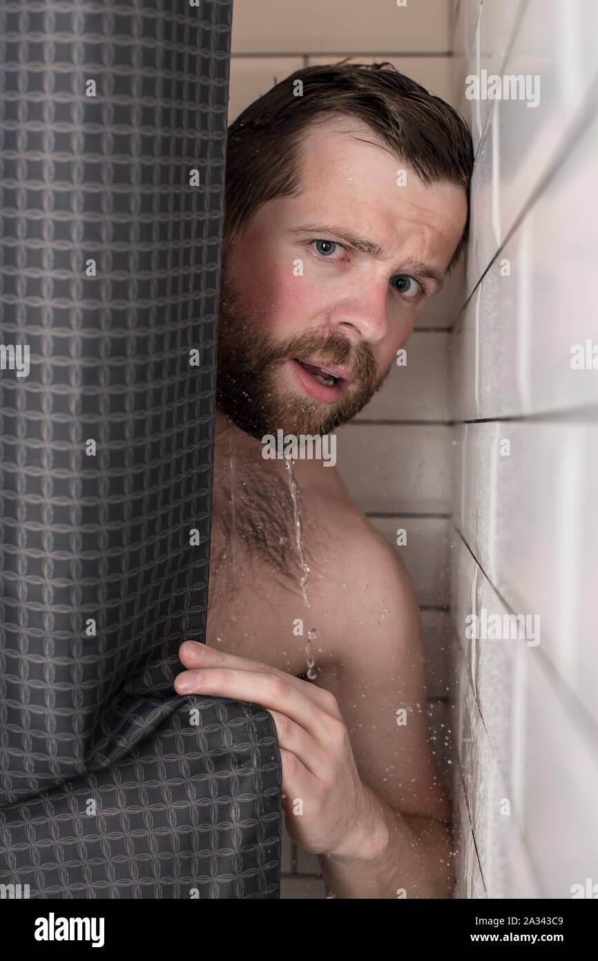 Gut aussehender, bärtiger Mann mit nassen Haar sieht aus hinter einem Vorhang in der Dusche. Close-up. Stockfoto