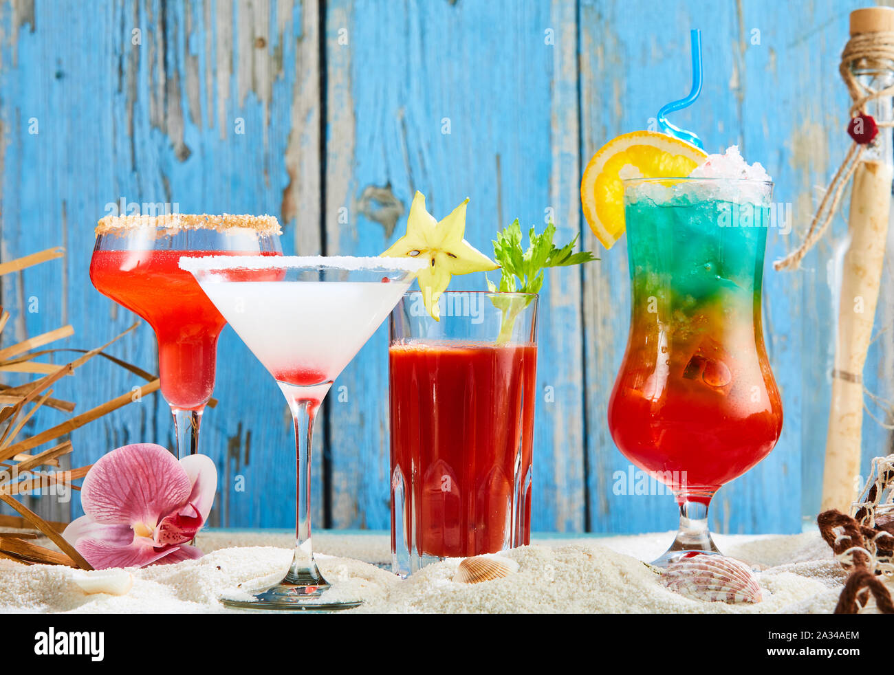 Sortierte bunte Cocktails mit einem Martini und Bloody Mary am weißen Strand Sand gegen eine rustikale verwittertem Blau Holz Hintergrund Stockfoto