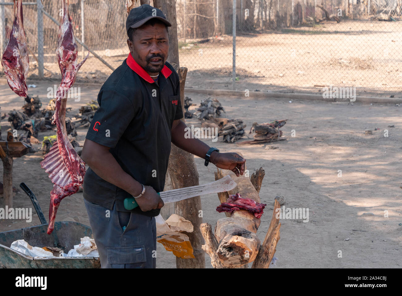 Opuwo, Namibia - 25. Juli 2019: Schwarzer Mann schlachten Ziege Fleisch auf einem traditionellen Markt mit Fleisch hängt im Hintergrund in Opuwo, Namibia Stockfoto