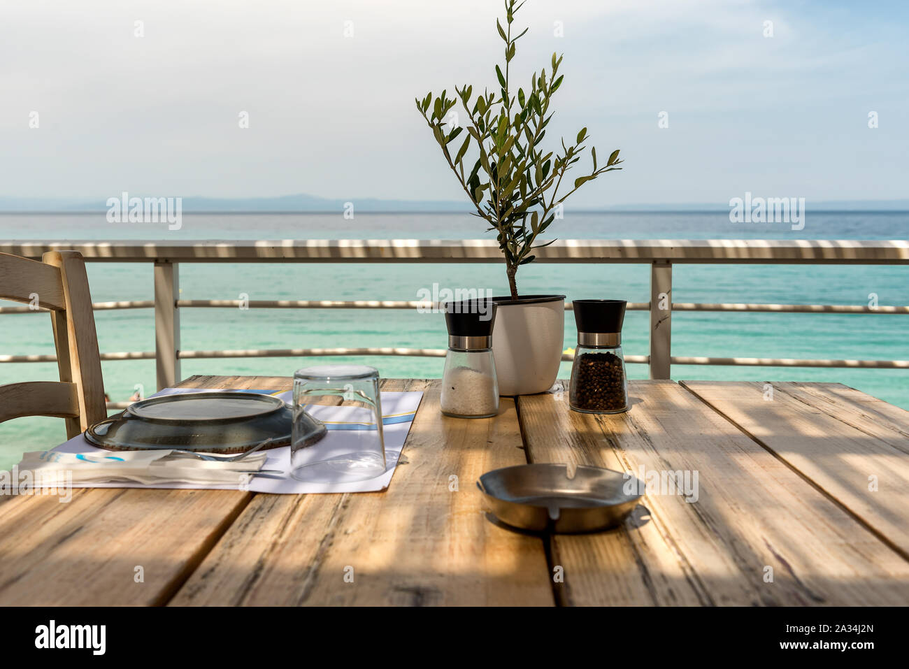 Mediterranes Restaurant Holztisch mit Olivenbaum, Setup, Salz und Pfeffer und Meerblick Stockfoto
