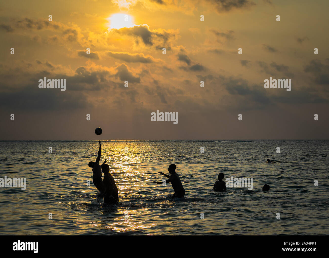 Silhouetted Gruppe von Jungen spielen eine Kugel in das Meer bei Sonnenuntergang Stockfoto