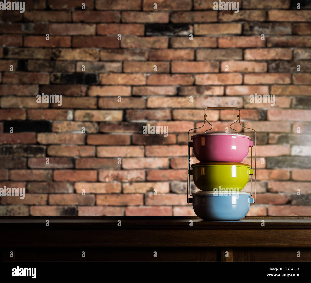 Bunte tiffin Carrier auf Holzschrank mit unscharfen Vintage brick wall gegen warmes Licht Stockfoto