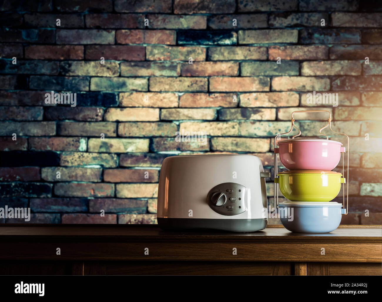 Bunte tiffin Träger und Toaster auf Holzschrank mit alten Mauer Hintergrund gegen warmes Licht Stockfoto