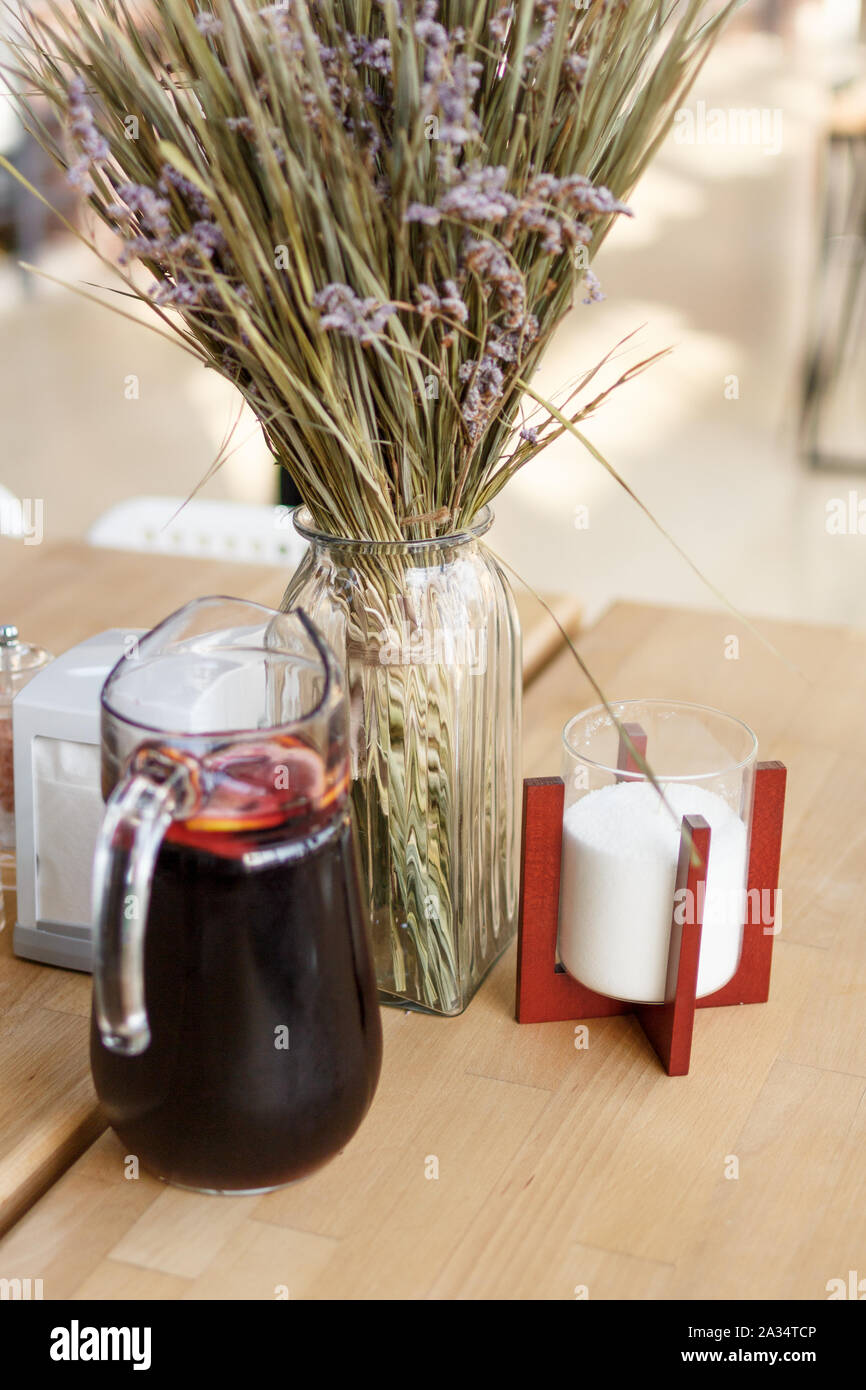 Sommer hausgemachte Dunkelrot Limonade mit frischen in Scheiben geschnittenen Zitronen in einer Kanne auf hölzernen Tisch. getrocknete Blumen Hintergrund Bouquet. Sonnigen Tag verschwommenen Hintergrund Stockfoto