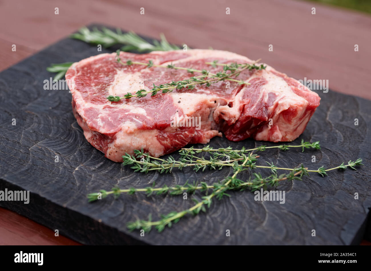 Raw Rib Eye Steak mit Kräutern auf Holzbrett Stockfoto
