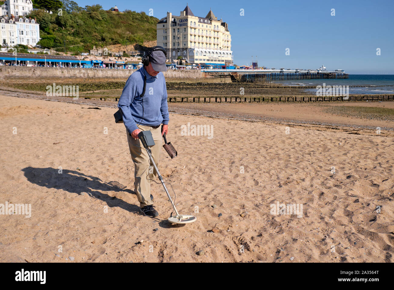 Mann im Herbst Outfit zu Fuß den Strand mit einem Metalldetektor auf der Suche nach Kostbarkeiten auf der Küstenstadt auf Llandudo, Wales. Stockfoto