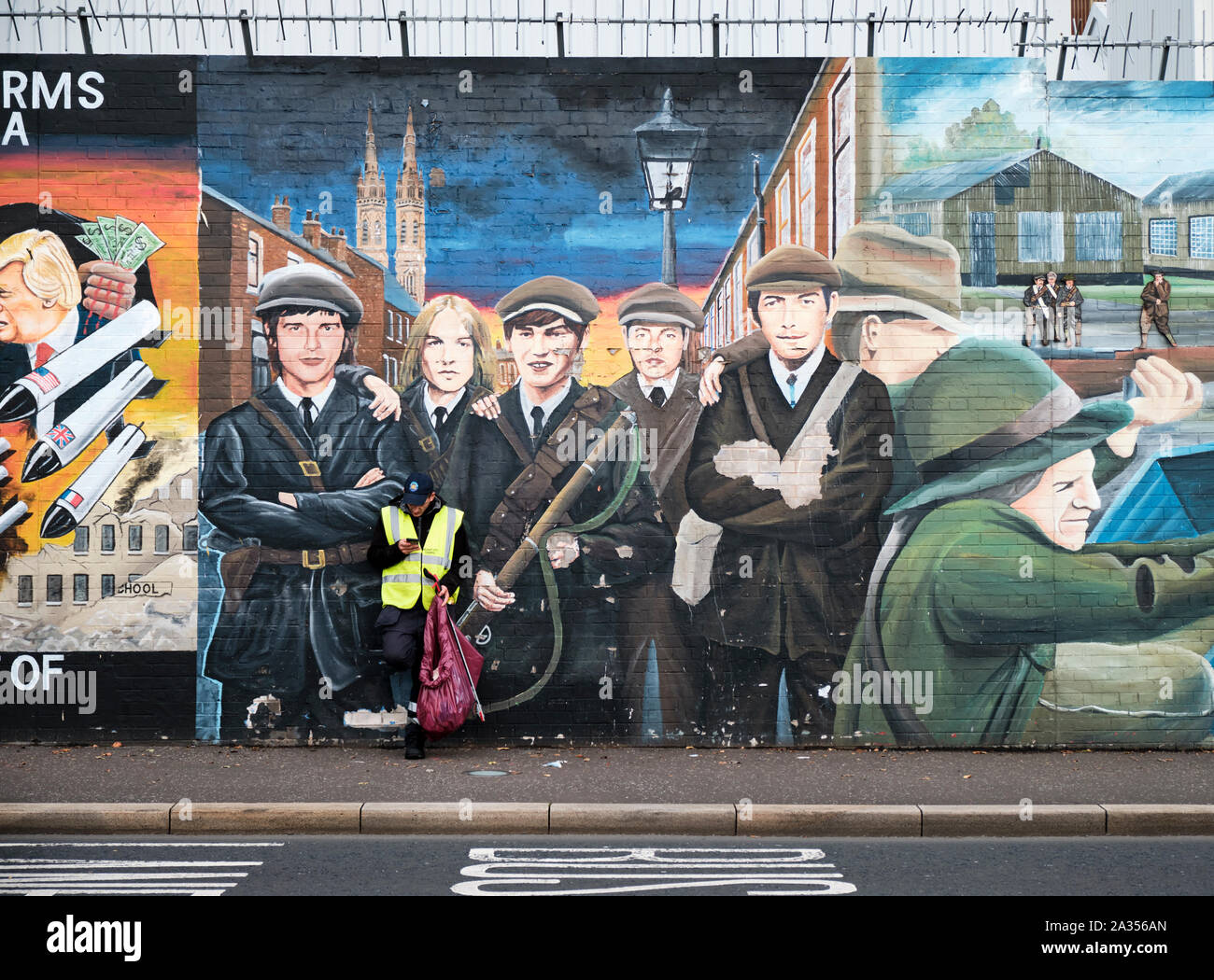 Städtische Mitarbeiter in der Pause auf seinem Mobiltelefon vor Wandmalereien auf den Frieden Wandbilder mit 'Lokale Freiwillige, Ausbildung" in Belfast, N Stockfoto