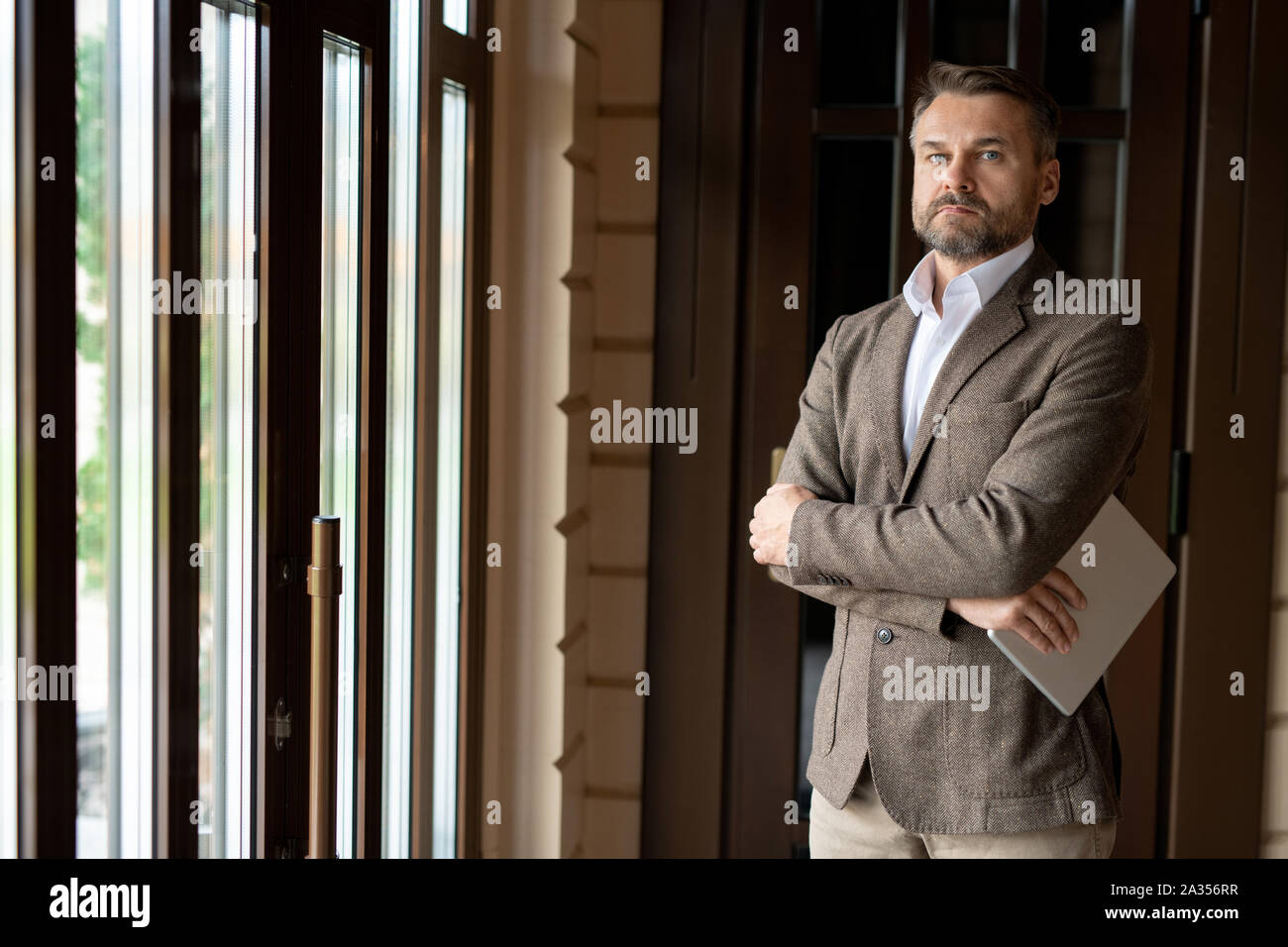 Schwere im mittleren Alter Führer mit Tablette suchen Sie im Stehen durch Fenster Stockfoto