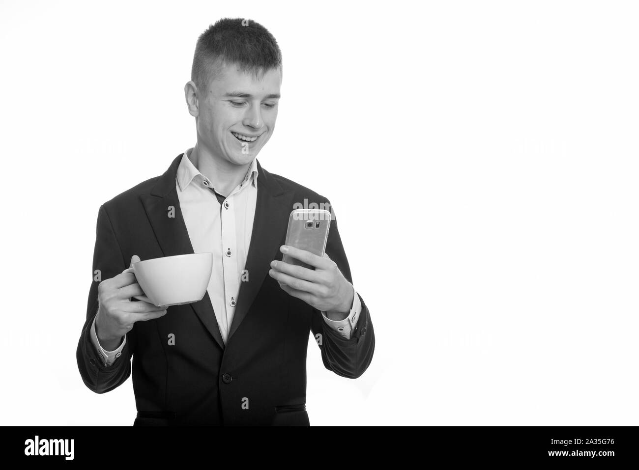 Studio shot der Jungen glücklich Geschäftsmann und lächelnd Kaffeetasse, während mit Handy Stockfoto
