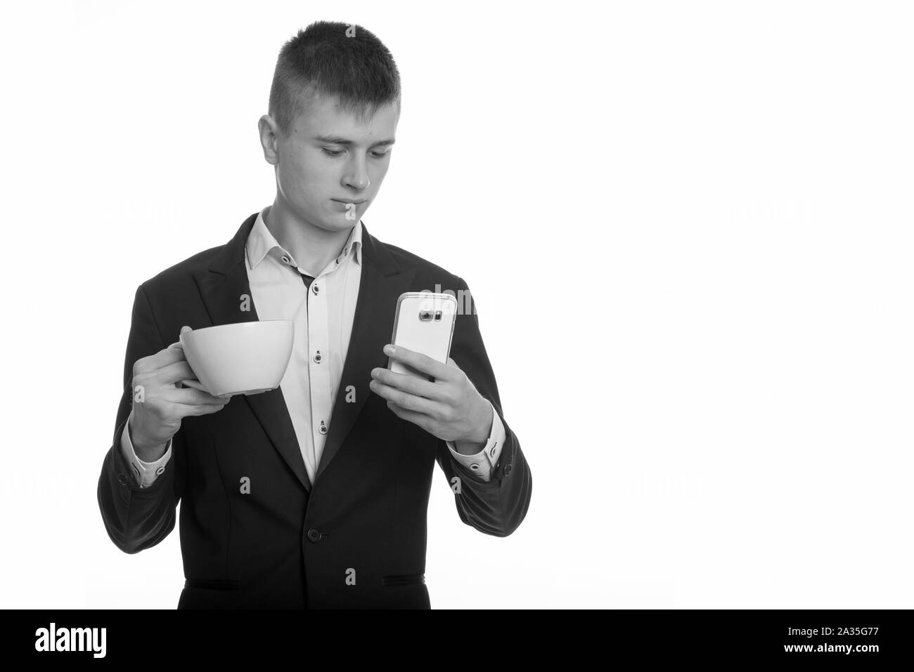 Studio erschossen der junge Geschäftsmann holding Kaffeetasse, während mit Handy Stockfoto