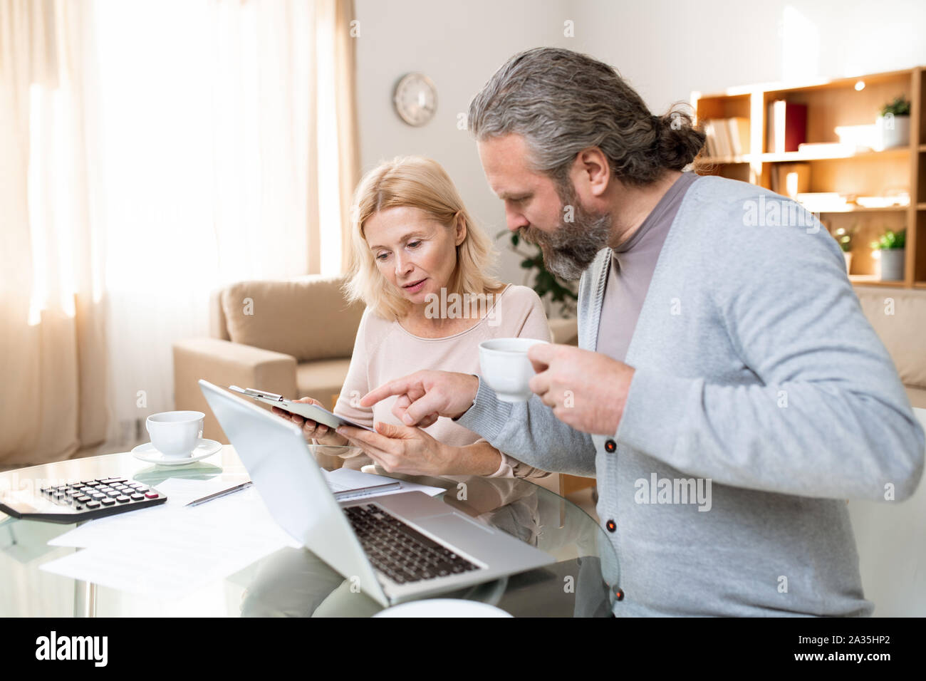 Reifen bärtiger Mann mit Tasse Tee in Dokument von seiner Frau gehalten, Stockfoto