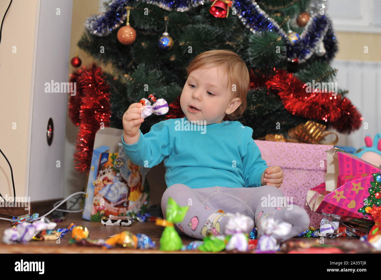 Das kleine Mädchen unter den Weihnachtsbaum. Baby Mädchen mit Geschenke unter dem Weihnachtsbaum. Stockfoto