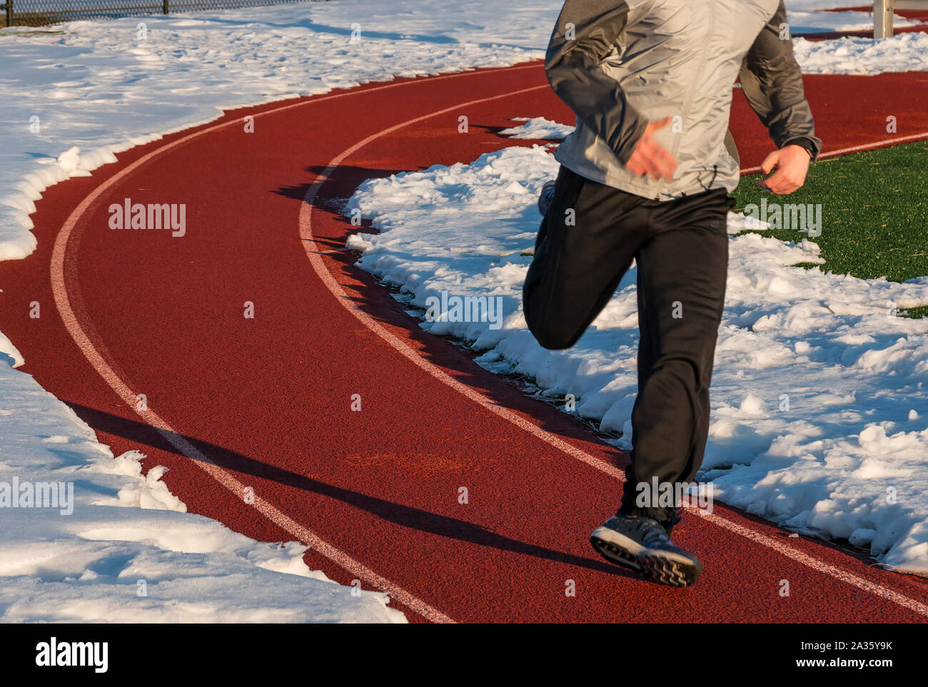 Ein Läufer läuft auf einer Schiene umgeben von schneebedeckten und ist über so schlecht pronating, es sieht so aus, als er seinen Knöchel rollt. Stockfoto
