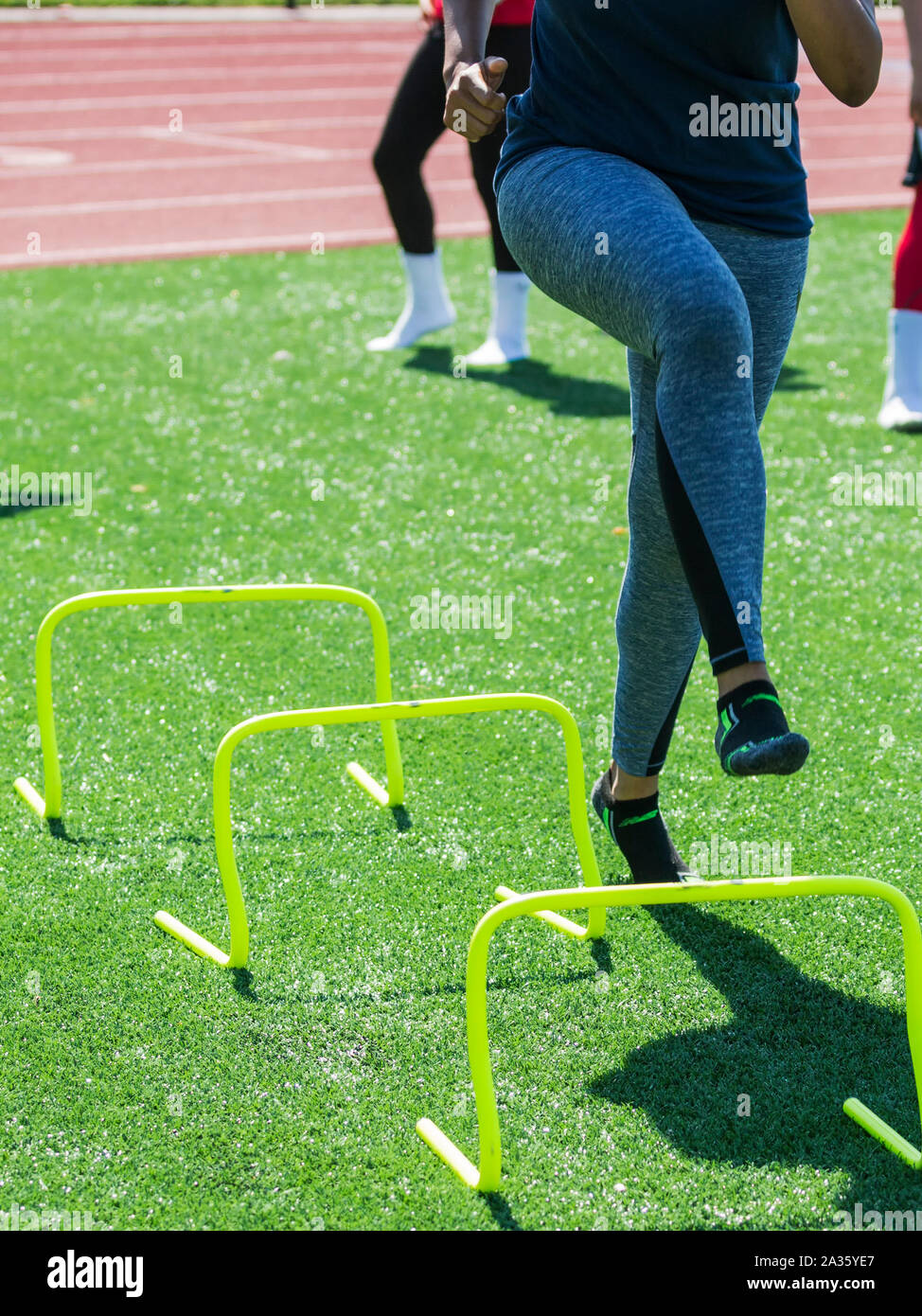 Ein Runner ist mit Online-schnelligkeitsübungen yovr Gelbe Mini Banane Hürden ohne Schuhe auf Während der Leichtathletik Praxis. Stockfoto