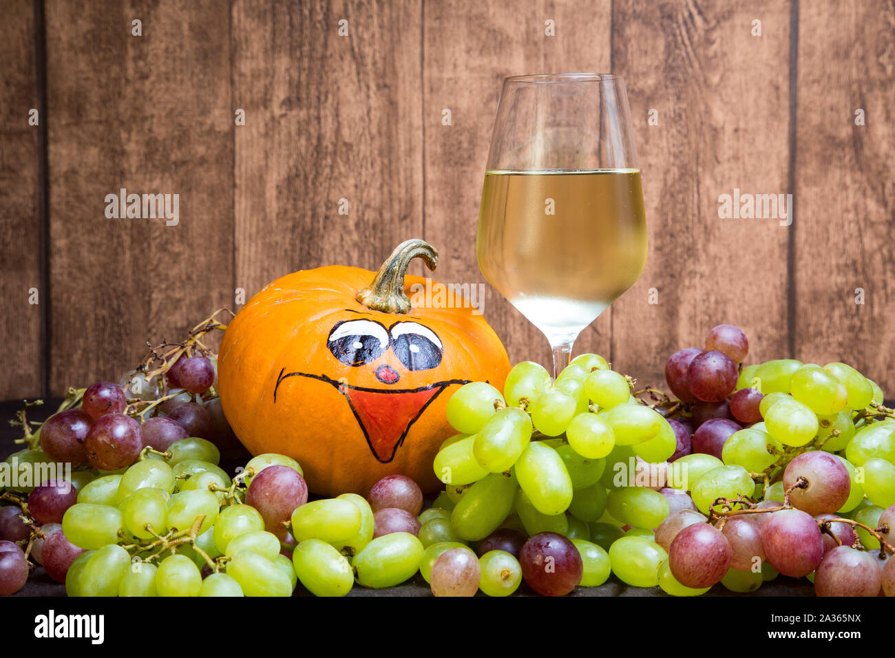 Glas Weißwein mit Kürbis und Weintrauben im Herbst. Imit einer natürlichen Holz- Platte als Hintergrund. Stockfoto