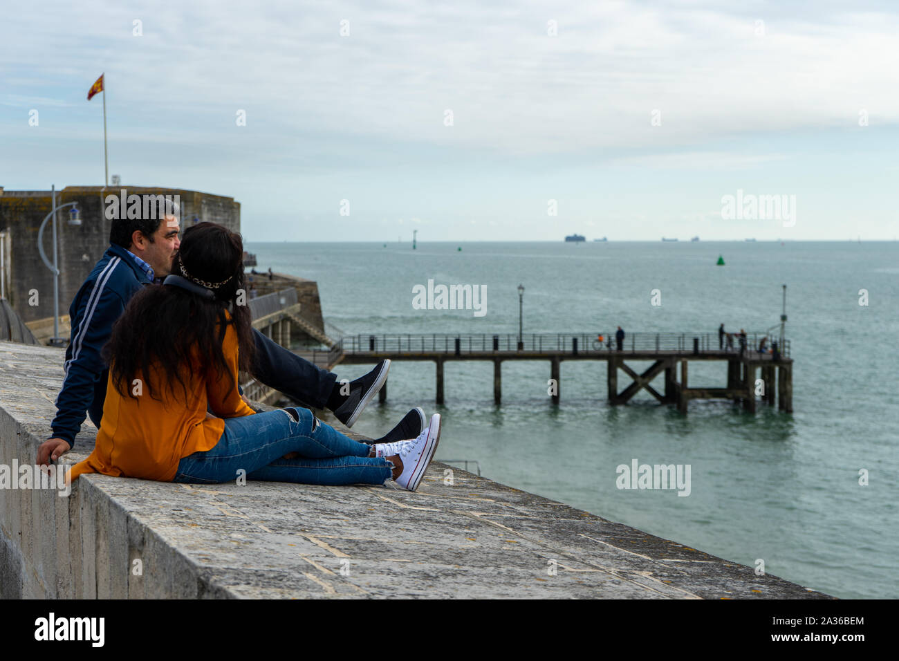 Eine multikulturelle Paare sitzen auf einer Mauer am Meer zu plaudern, während mit Meerblick an der Ansicht Stockfoto