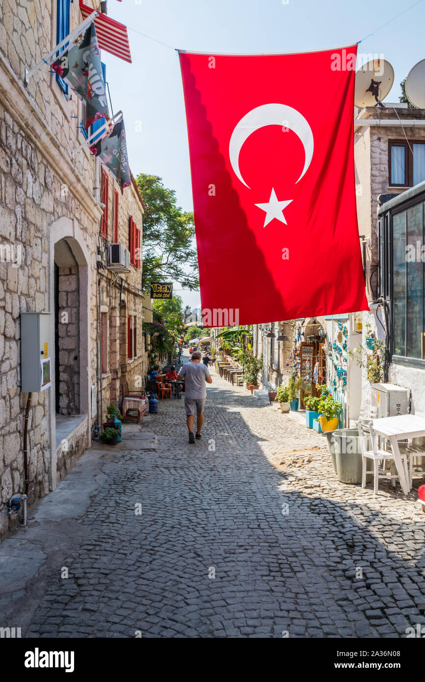 Alacati, Türkei - September 2019: Ein Mann geht eine Straße die Türkische Flagge. Viele Touristen besuchen die Stadt. Stockfoto