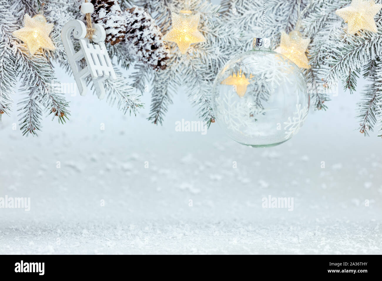 Winter Hintergrund mit schneebedeckten Tannenbaum Zweig mit Glaskugel dekoriert, Holz- schlitten, Sterne leuchten Girlanden Stockfoto