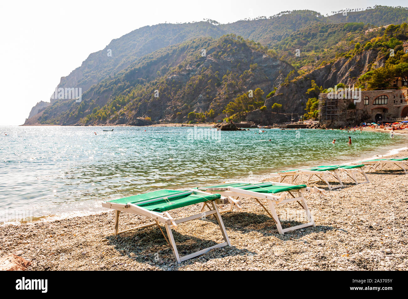 Monterosso al Mare, Italien - September 02, 2019: Grüne Liegestühle auf Kieselstrand mit grünen Bergen im Hintergrund in Monterosso, Cinque Stockfoto